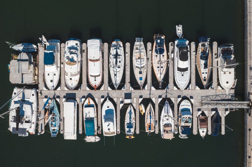 Drone shot capturing yachts and boats docked in a marina harbor from above.